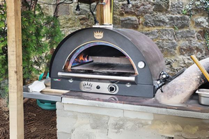 An image of a pizza oven outdoor lit and sat on a kitchen work top.