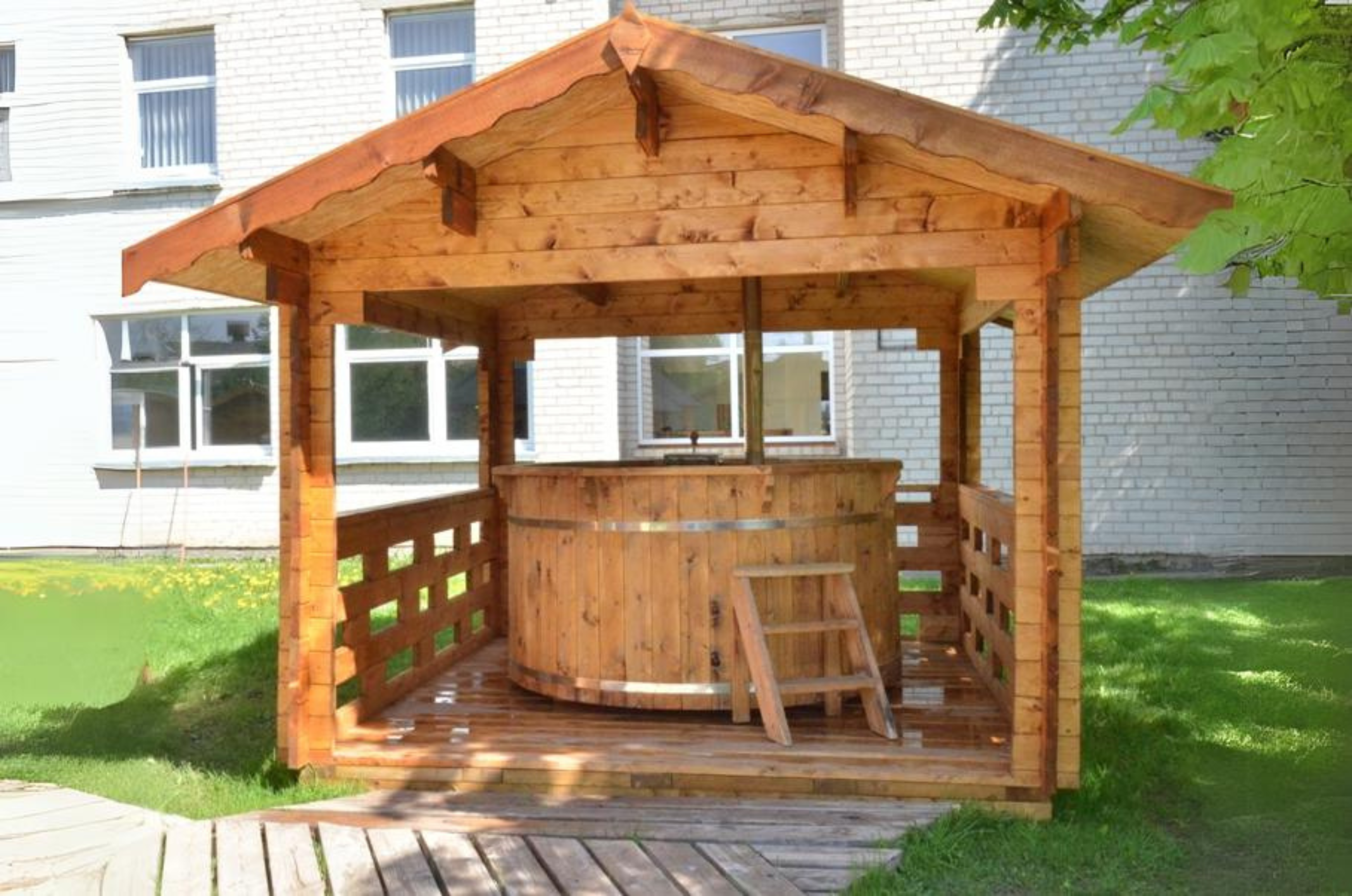 A wooden structure with roof and ventilation surrounds a 6 person hot tub with spruce steps for entry.