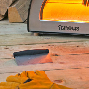 A close up shot of the igneus dough cutter lay on wooden surface in front of a lit pizza oven