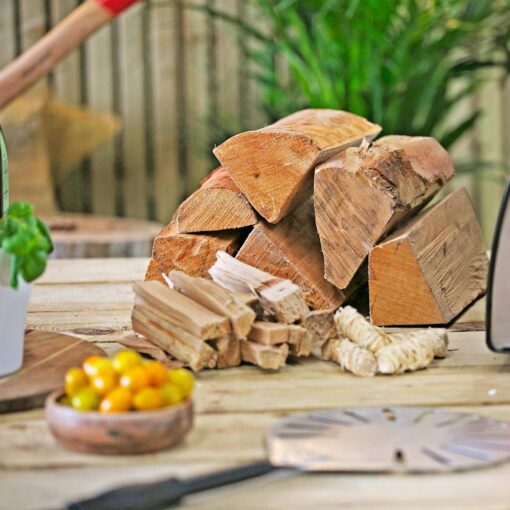 The wood bundle collection showing natural firelighters, kindling, and the wood for the pizza ovens on top of a wooden table with some tomatoes and a pizza spinner in front