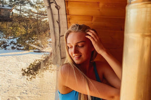 A close up image of the glass backed sauna barrel with a woman sat inside and the snowy garden in the background.