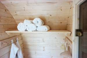 An interior shot showing the changing room shelf with towels atop and the clothes hangers with the glass entrance door to the sauna to the right.