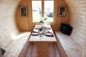 the dining area within the sauna barrel, table set for dinner, benches for up to 6 people and a glass windowed back.