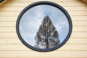 A close up shot of a sauna barrel window showing a reflection of a tree in the background.