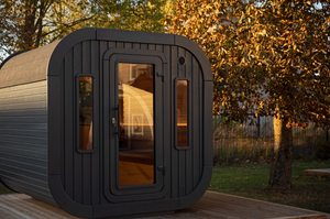 A angle shot of the black Luna sauna closed - showing the front of the cabin with a tree to the right.