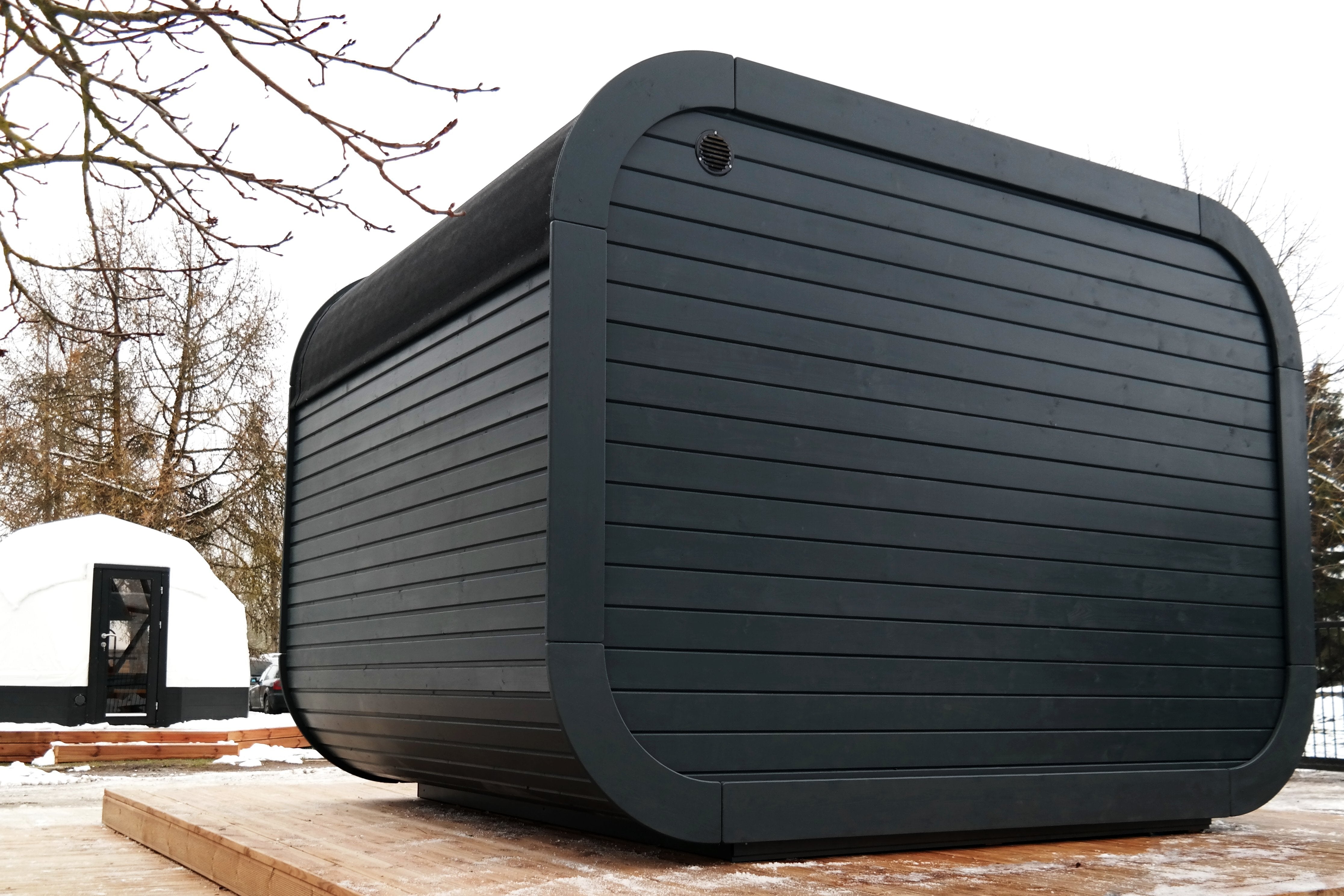 An image showing the back of the black Sauna with ventilation top left with the structure atop a wooden terrace.