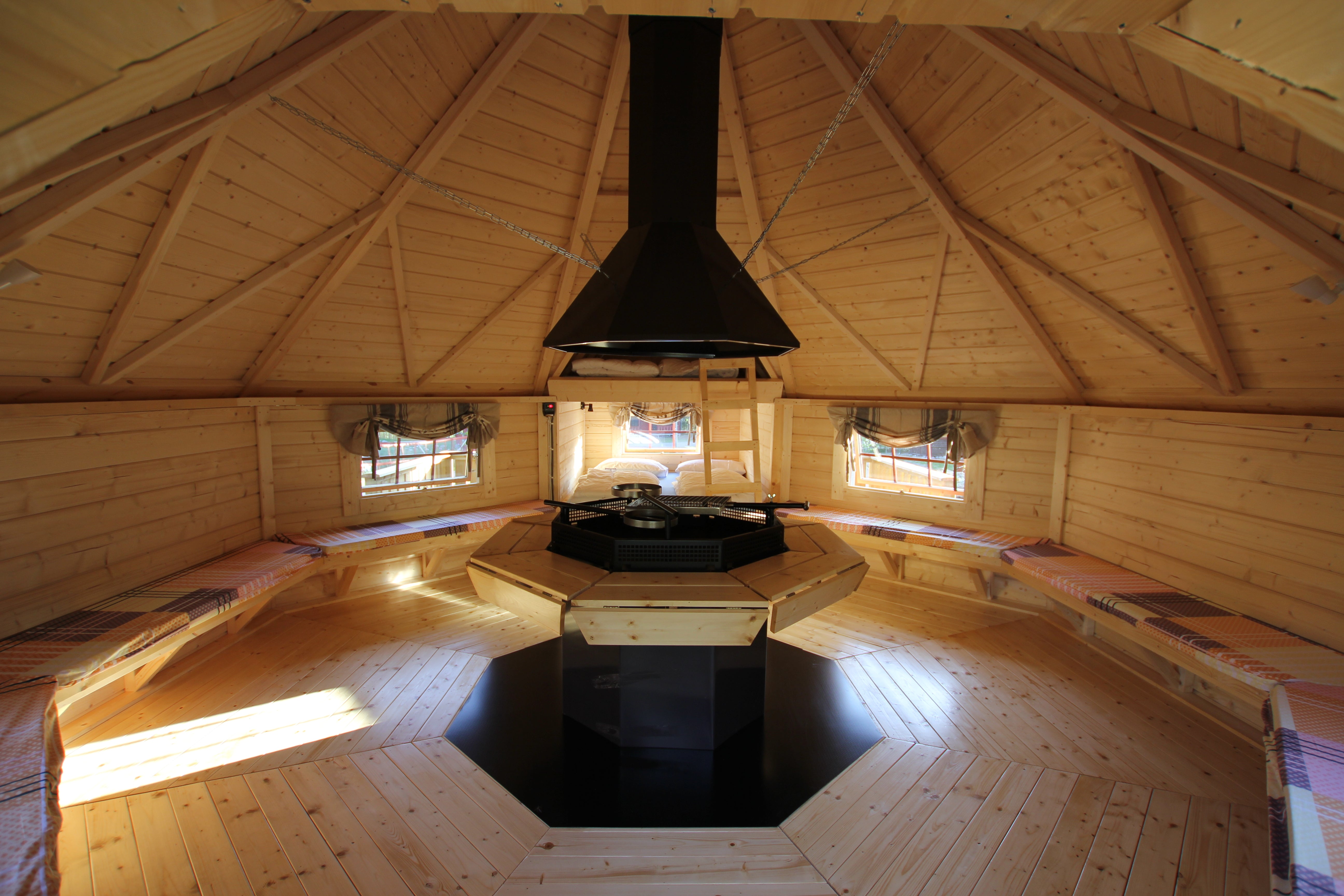 The interior of the BBQ Hut with exposed wood sloping roof and benches lining the walls - the BBQ itself sits in the centre