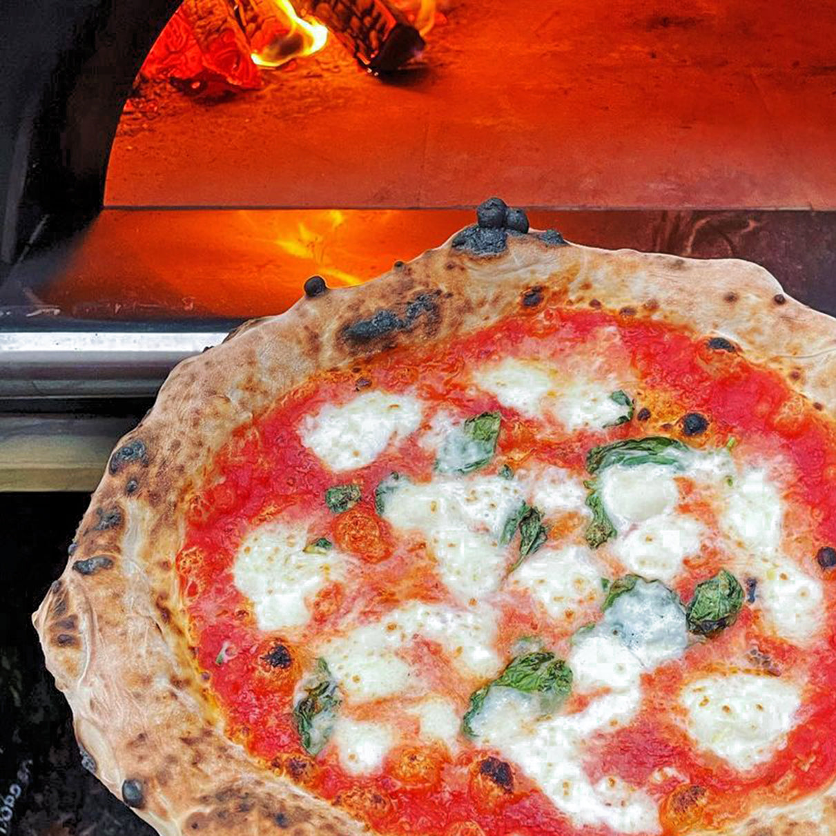 A close up image of pizza just pulled from a woodfired pizza oven.