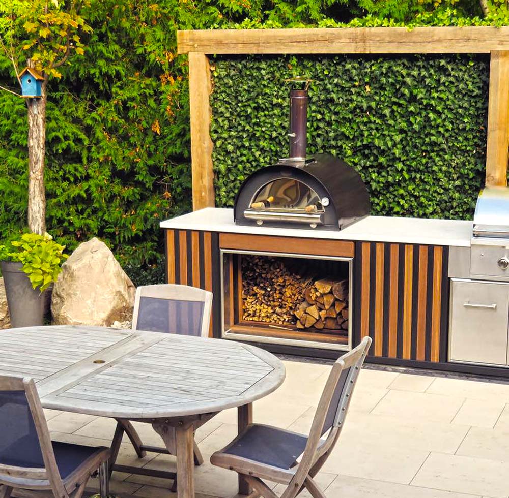 A black sided pizza oven atop a outdoor kitchen worktop.