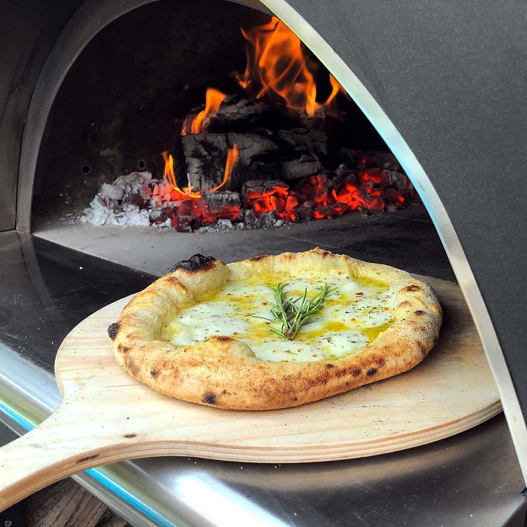 A cooked pizza being pulled out of a lit woodfired BBQ pizza oven.