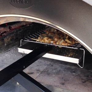 Clementi Pizza Oven, lit with wooden logs burning low to the left of the oven, uncooked kebabs atop the multicook system situated within the oven.