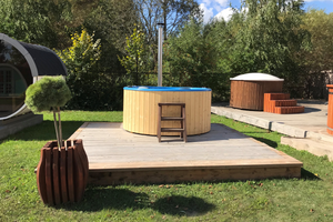 The Fiberglass Hot Tub atop a wooden terrace in a grass-filled garden, between another hot tub and a sauna