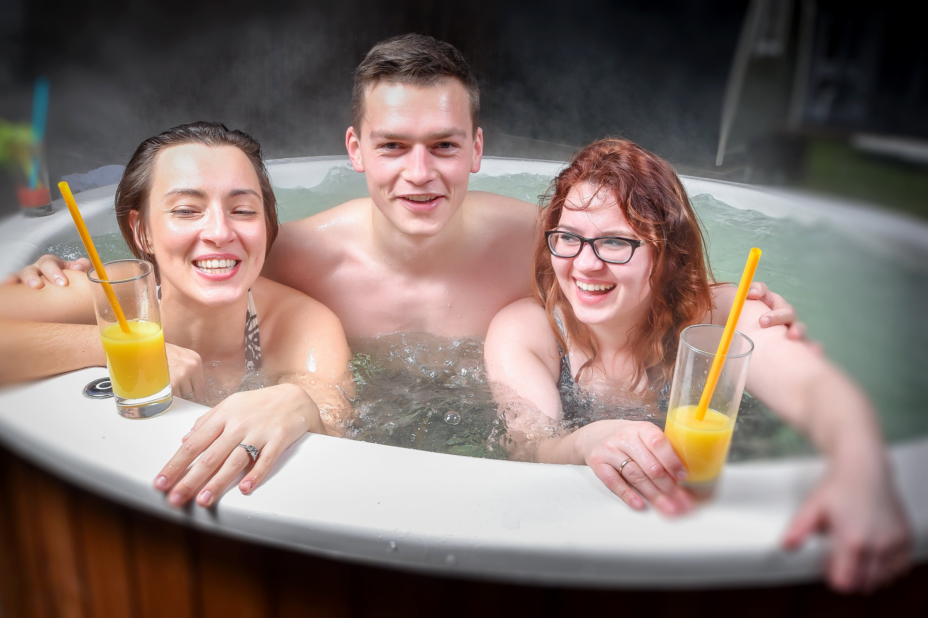 A group of three friends drinking juice and laughing in the Fiberglass Hot Tub