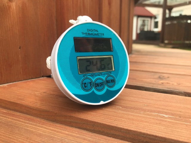 A blue topped digital thermometer for hot tubs lay on wooden decking showing the heat display and the button options