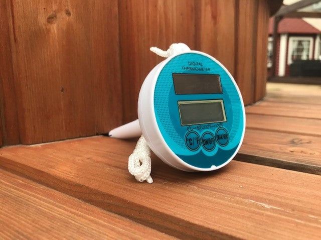 The blue top digital thermometer for hot tubs lay on wooden decking in a side profile view showing the length of the product.