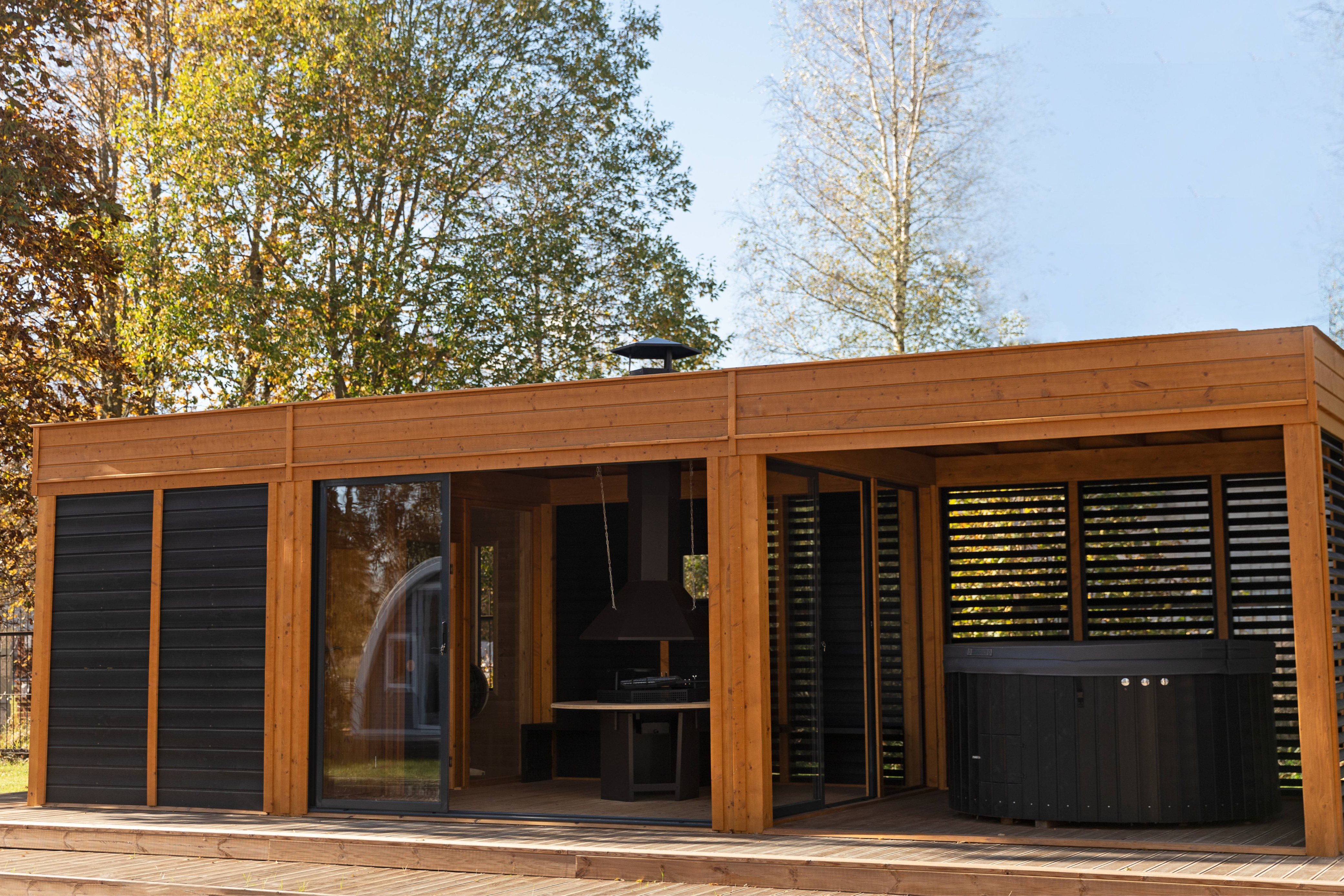 The Garden Cube in pine (wood stain) with sauna in the left sector, BBQ table in the centre and hot tub in the right