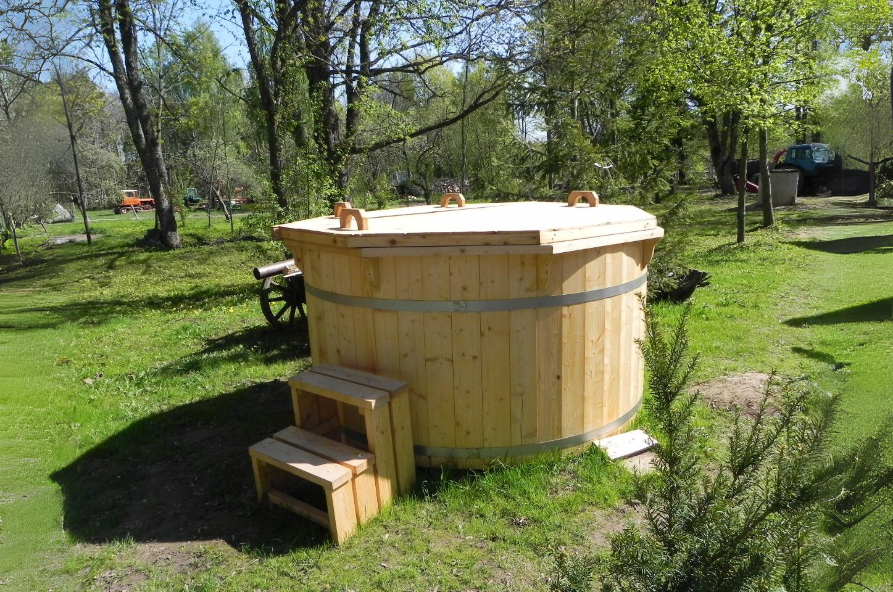 a light oak finished hot tub with wooden spruce cover sat on some grass in a lovely garden scape.