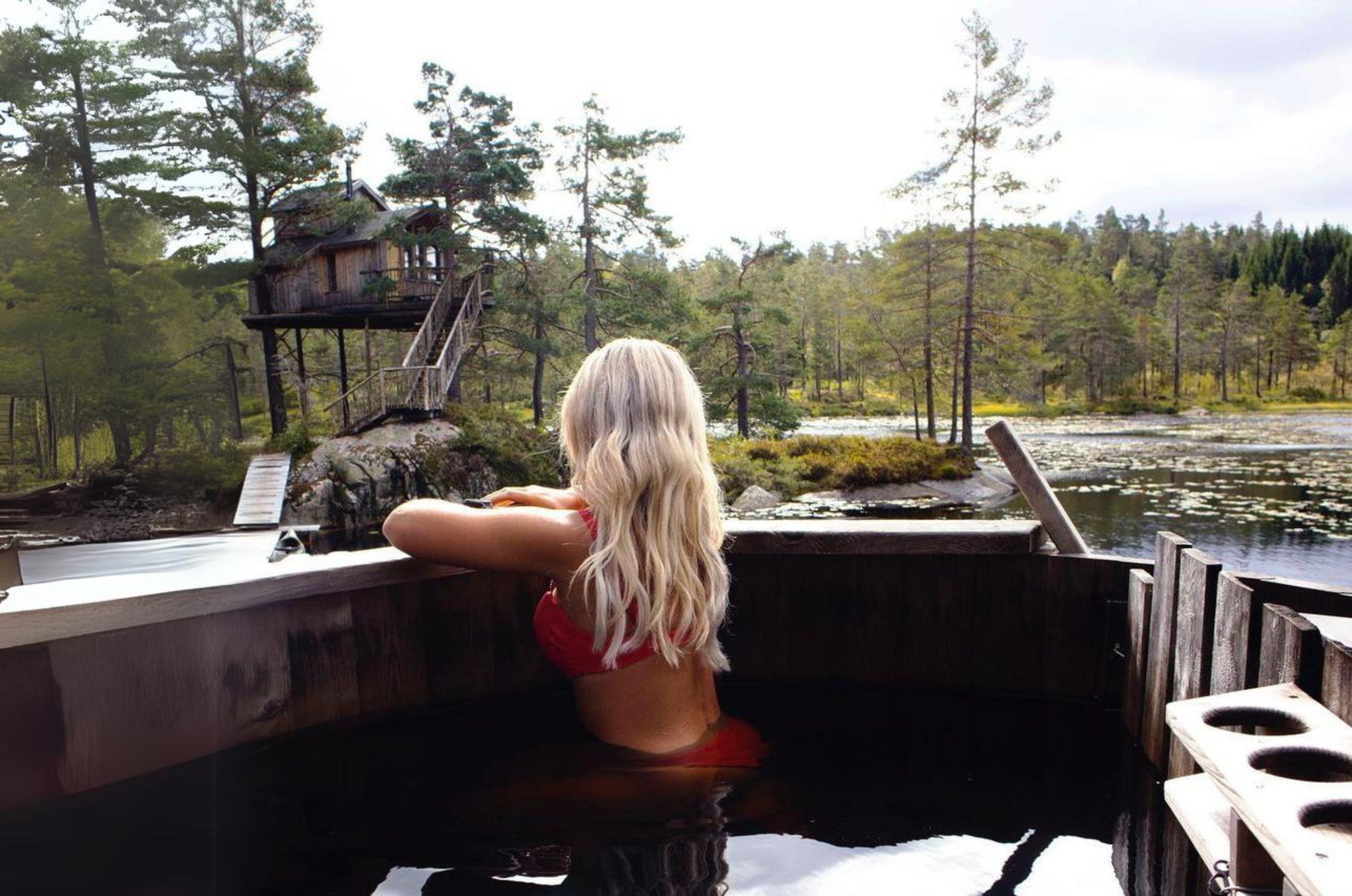 A lady sat in the 6 person hot tub facing away looking at the trees and lake in the background.