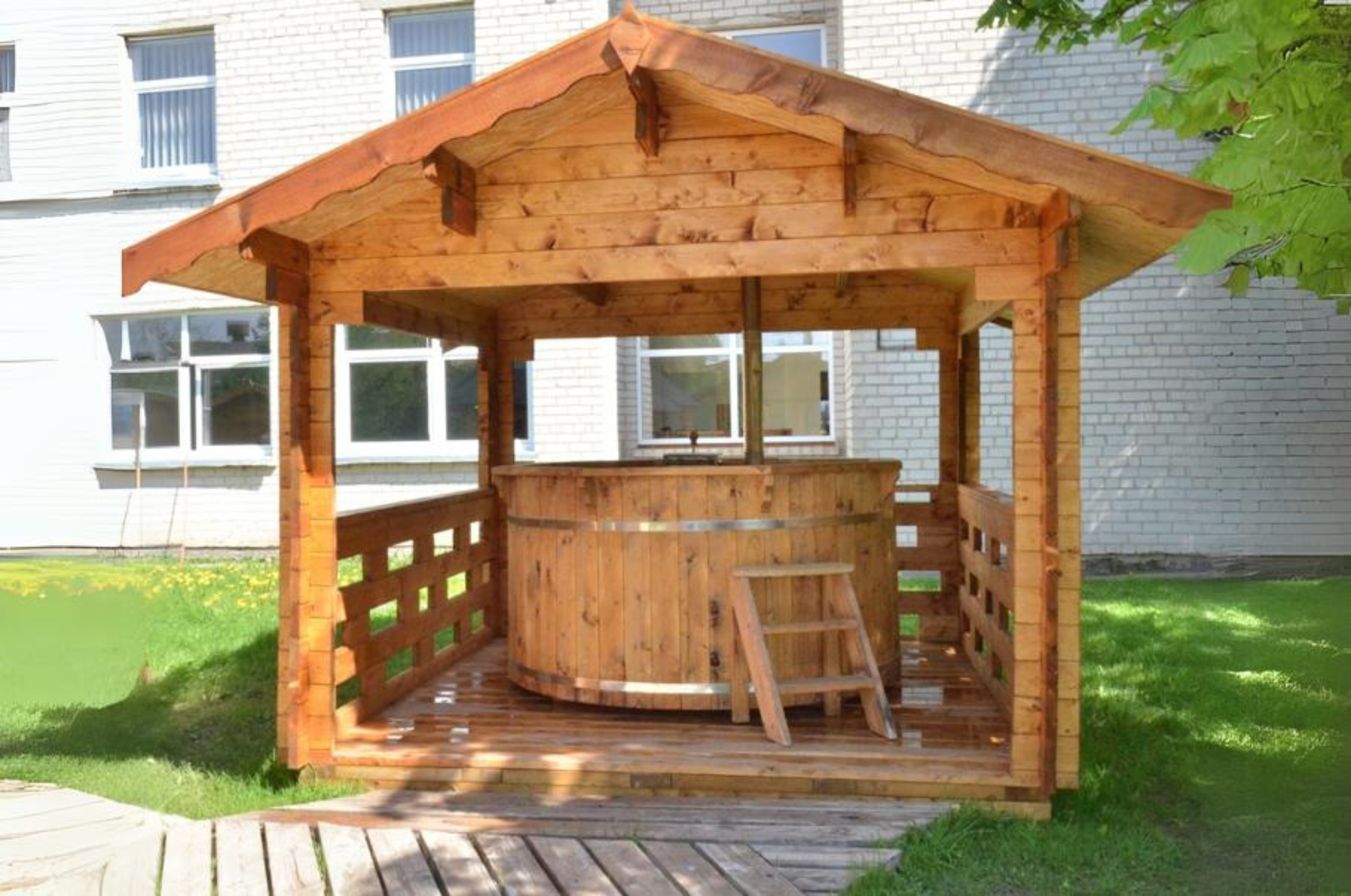 A wooden structure with roof and ventilation surrounds a 6 person hot tub with spruce steps for entry. 