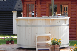 A side on photo showing an 8 person hot tub with interior wooden heater and spruce steps sat on top of a wooden terrace with a BBQ hut in the background.