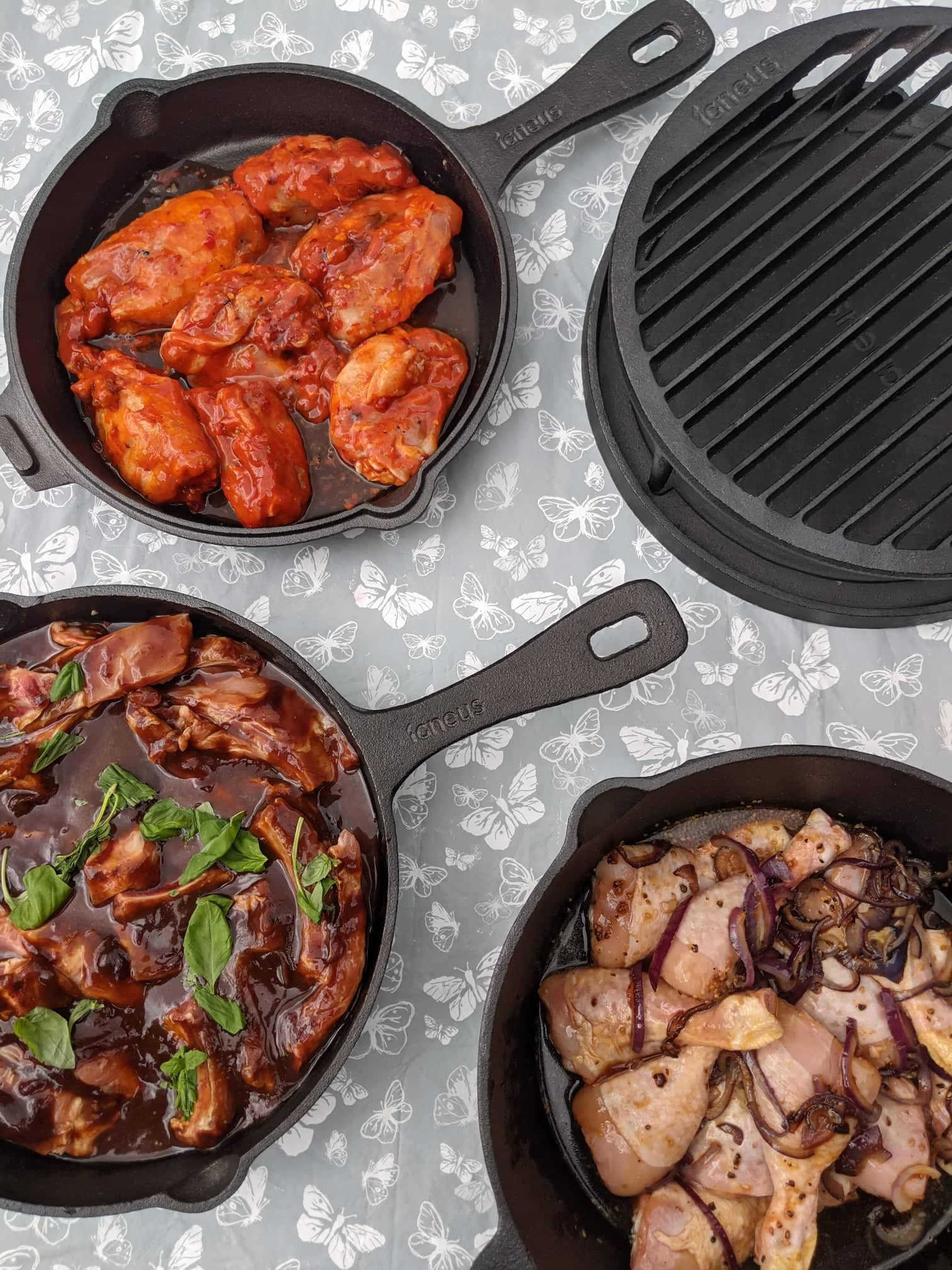 A top down photograph of the igneus 3 part cast iron set and the tuscan grill - the 3 part set shows the cooking options with an assortment of seasoned chicken dishes, vegetables and marinades 