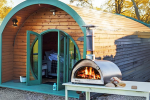 The Bambino wood fired pizza oven outdoor on a table in-front of a large wooden cabin