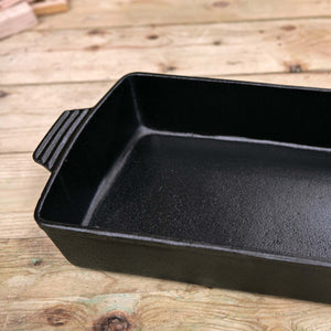 A black cast iron roasting dish in a top down photo shot showing the nice depth of the product on a wooden table top