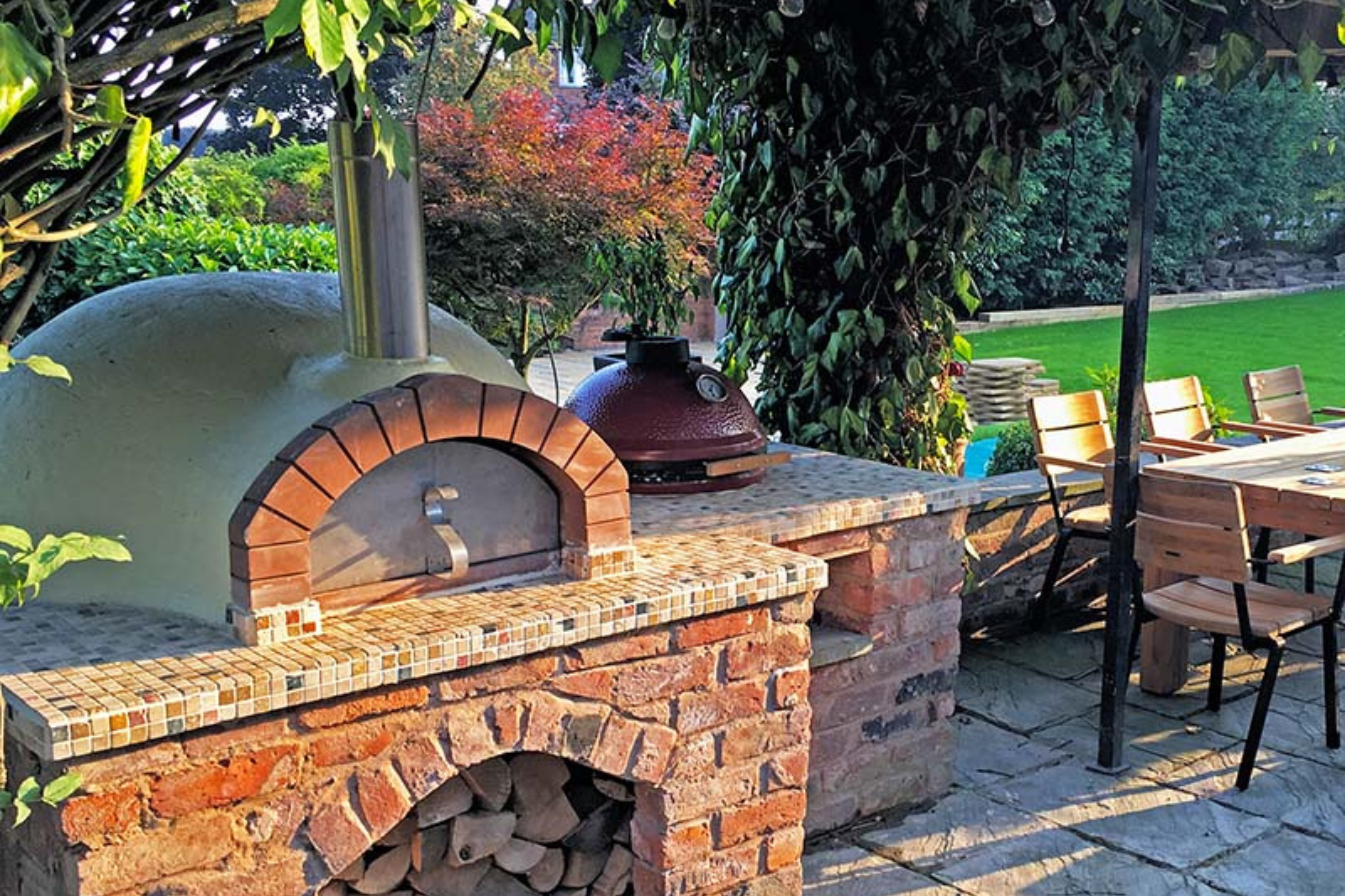 Pizza ovens, including the Ceramiko Pro 1000 outdoor pizza oven, built onto a brick table in a large modern garden