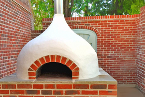 The Ceramiko Pro 1000 wood fired pizza oven outdoor on a brick table nestled within brick walls