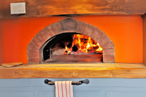 The Ceramiko Pro 1000 bbq pizza oven exterior built into a wall with a natural wooden table