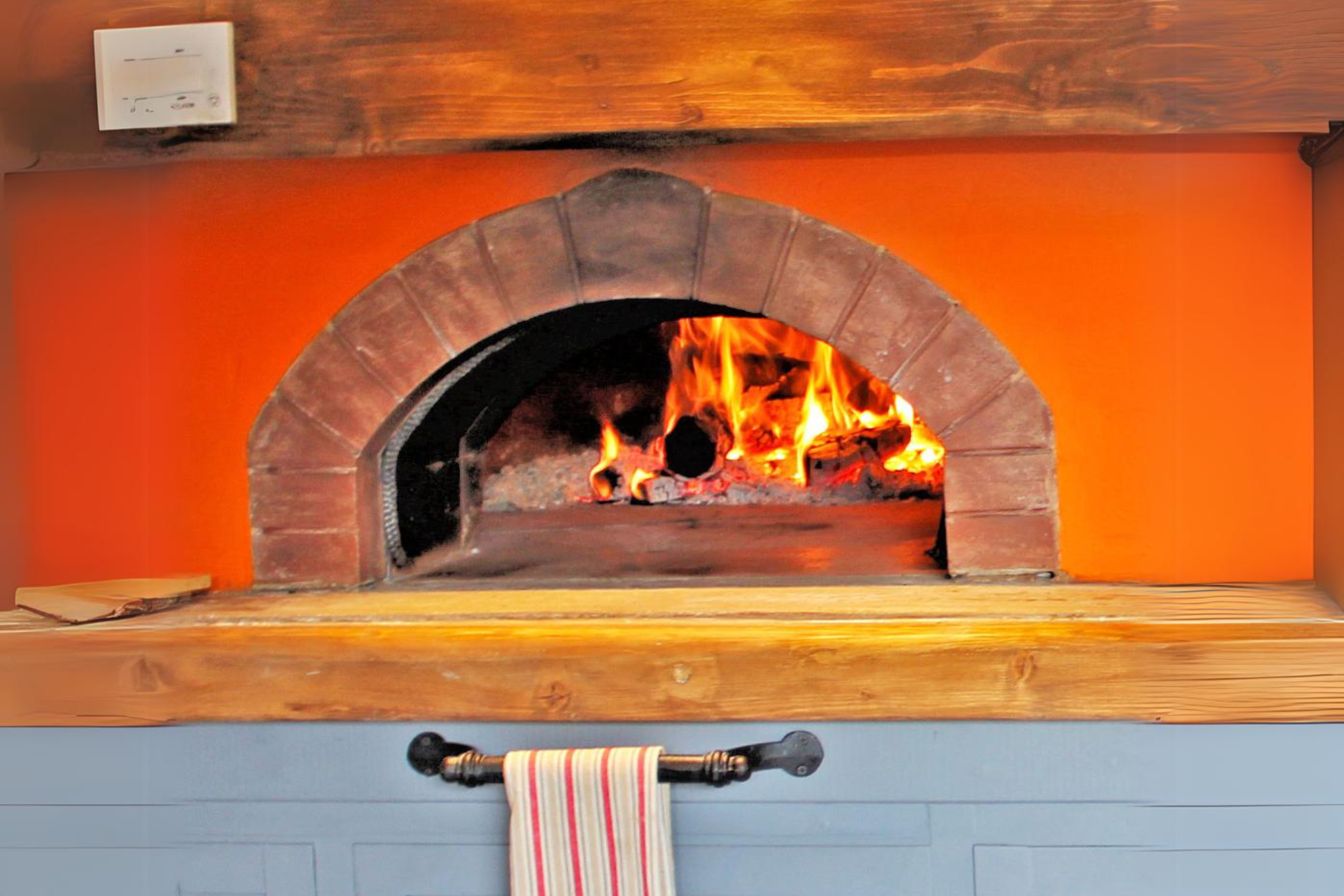 The Ceramiko Pro 1000 bbq pizza oven exterior built into a wall with a natural wooden table