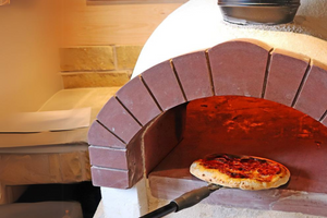 The Ceramiko Pro 1200 garden pizza oven exterior in a brick-walled alcove. A pizza cooking inside