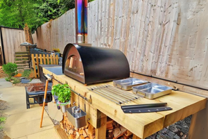 The Classico bbq pizza oven exterior in black atop a wooden table in a quaint garden