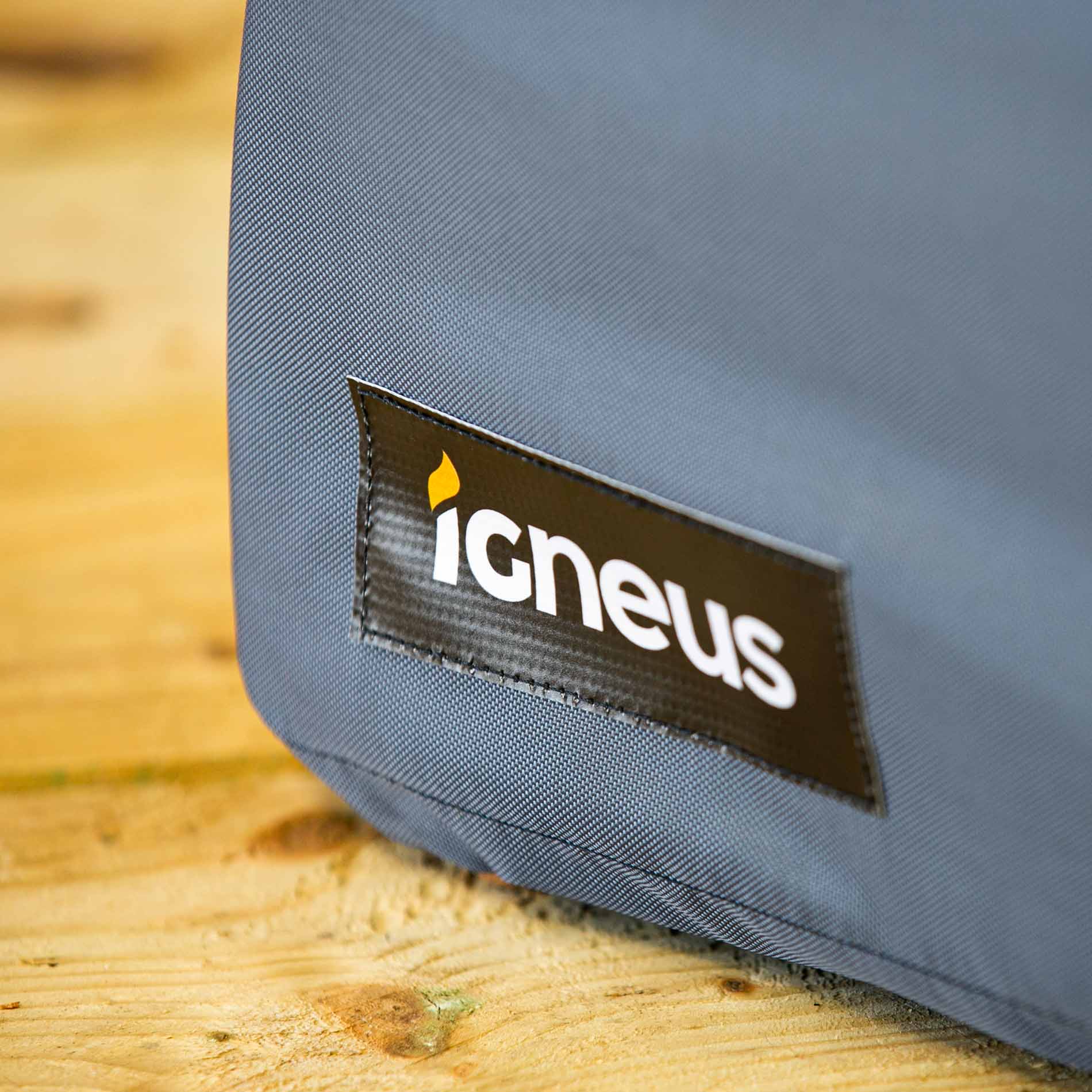 A close up shot of the Igneus pizza oven cover showing the logo sewn onto the cover placed on a wooden work top.