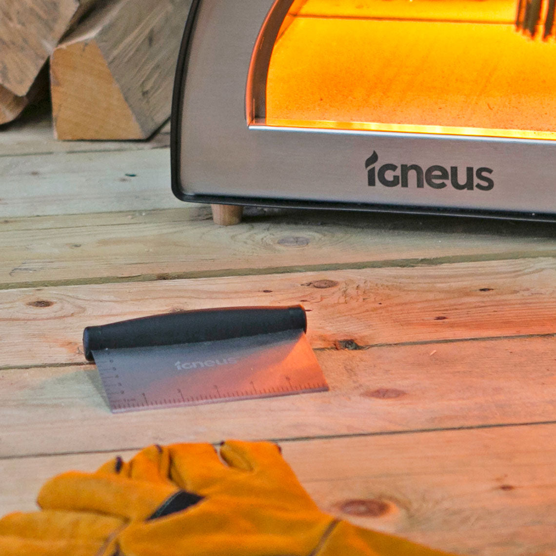 A close up shot of the igneus dough cutter lay on wooden surface in front of a lit pizza oven