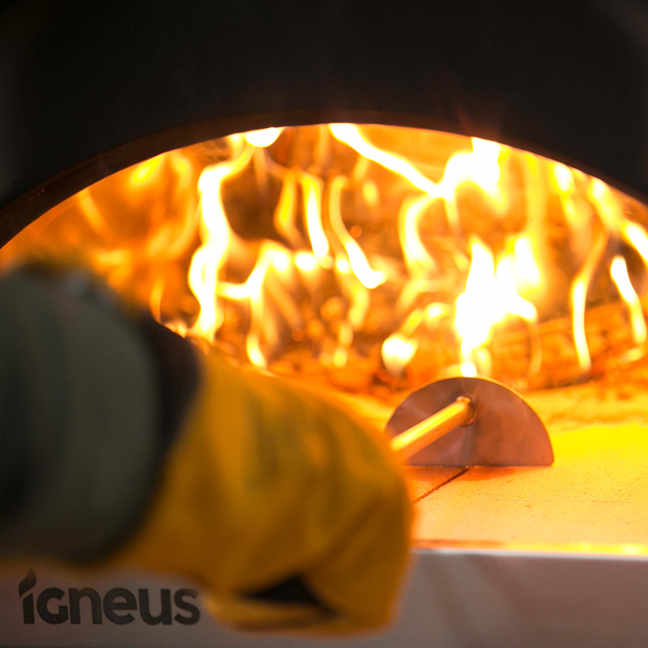 A photo of the igneus pizza oven rake in action being used on a lit pizza oven