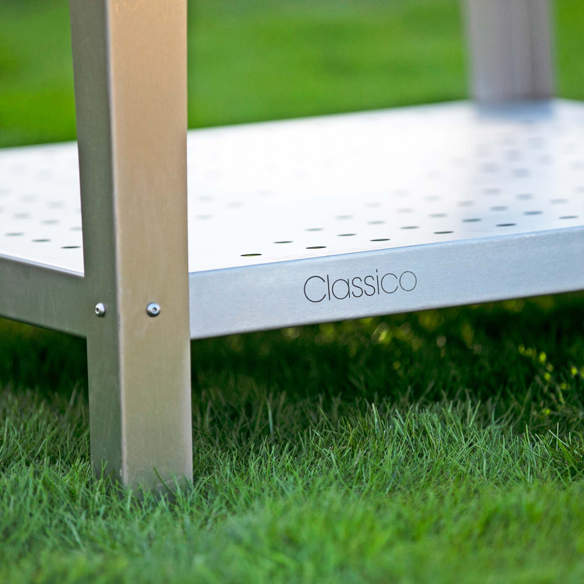 A close up shot of the classico logo on the base of a silver pizza oven outdoor stand on some grass