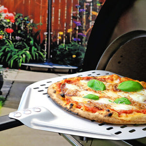 A cooked pizza being removed from an igneus pizza oven outdoor, with a modern garden in the background of the image