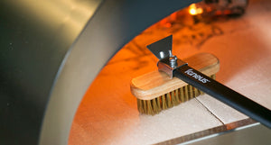 The igneus pro brush in action brushing the firebricks inside a lit igneus BBQ pizza oven.