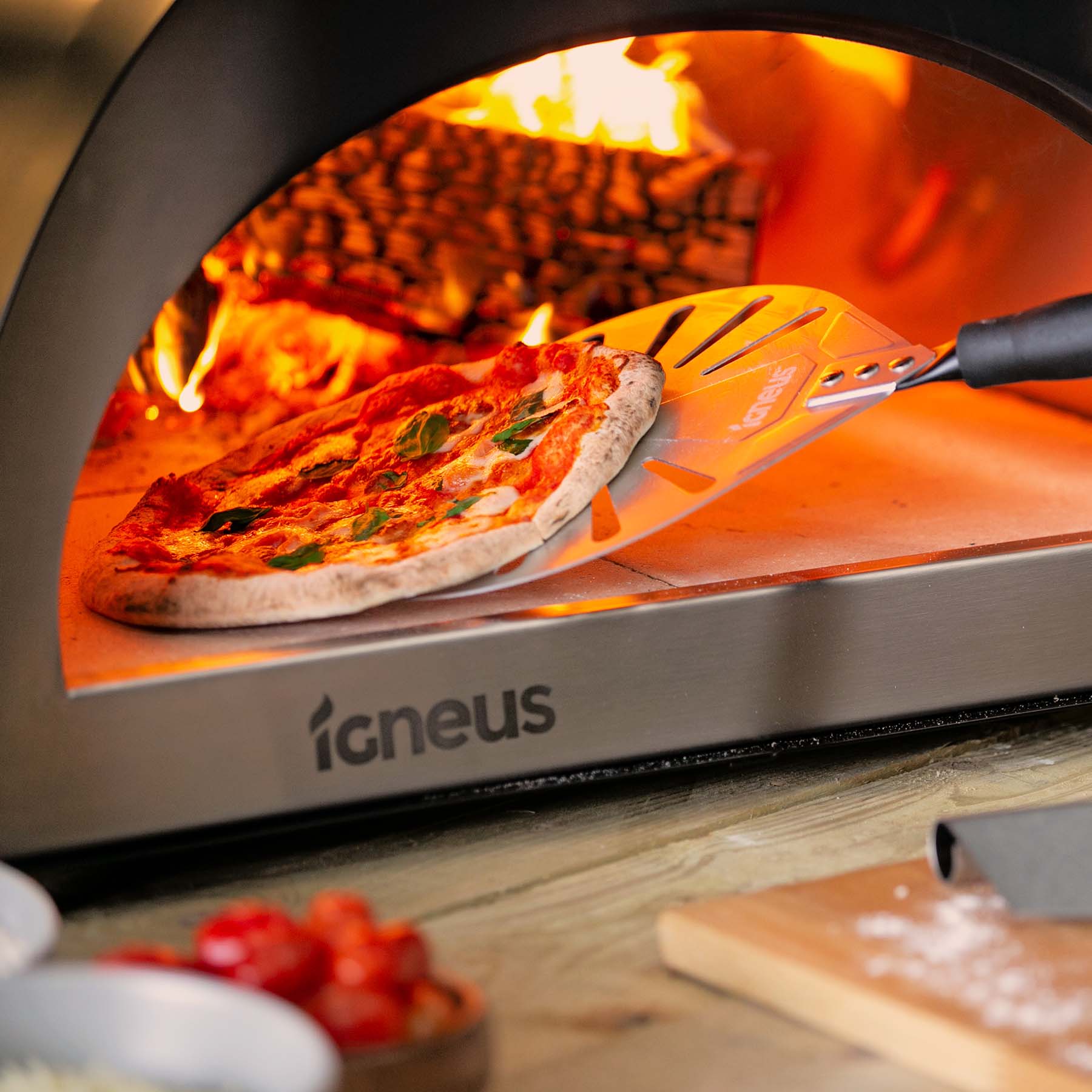 A lit pizza oven with a pizza being taken out of it by the Igneus Pro Pizza Oven spinner