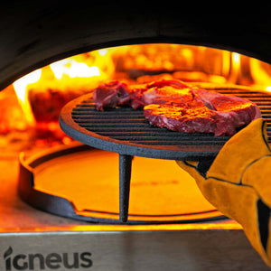 A steak is ontop of the igneus tuscan grill being placed into a lit pizza oven