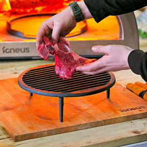 A well seasoned steak is being placed atop the igneus tuscan grill in preparation to be placed into the igneus pizza oven