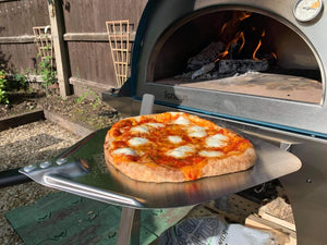 A lit pizza oven with a pizza being removed using the pizza peel