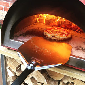 A pizza being placed back into a lit pizza oven outdoor using the Igneus pizza oven peel