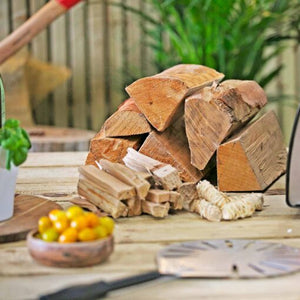 The wood bundle collection showing natural firelighters, kindling, and the wood for the pizza ovens on top of a wooden table with some tomatoes and a pizza spinner in front