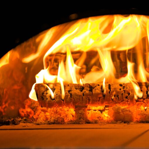 The logs from the pizza oven wood bundle being show inside of a BBQ pizza oven and they are lit.