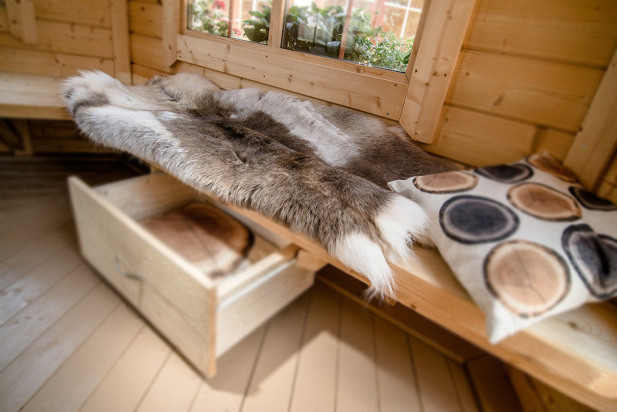 A image of a reindeer hide on a bench inside one of the BBQ huts from Viking Industrier a draw below for storage and a cushion to it's right.