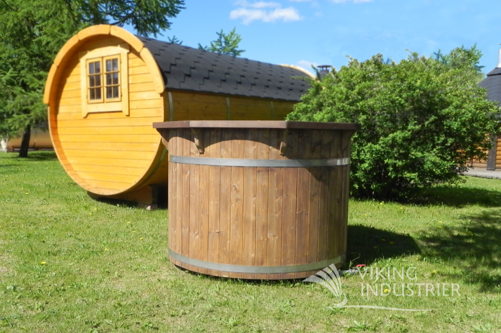 A spruce cold tub with dark oak finish sat on some grass in front of a sauna barrel.