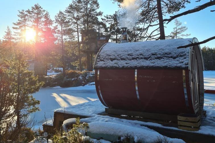 A sauna barrel on a wooden frame encapsulated by a snowy garden and trees in the background