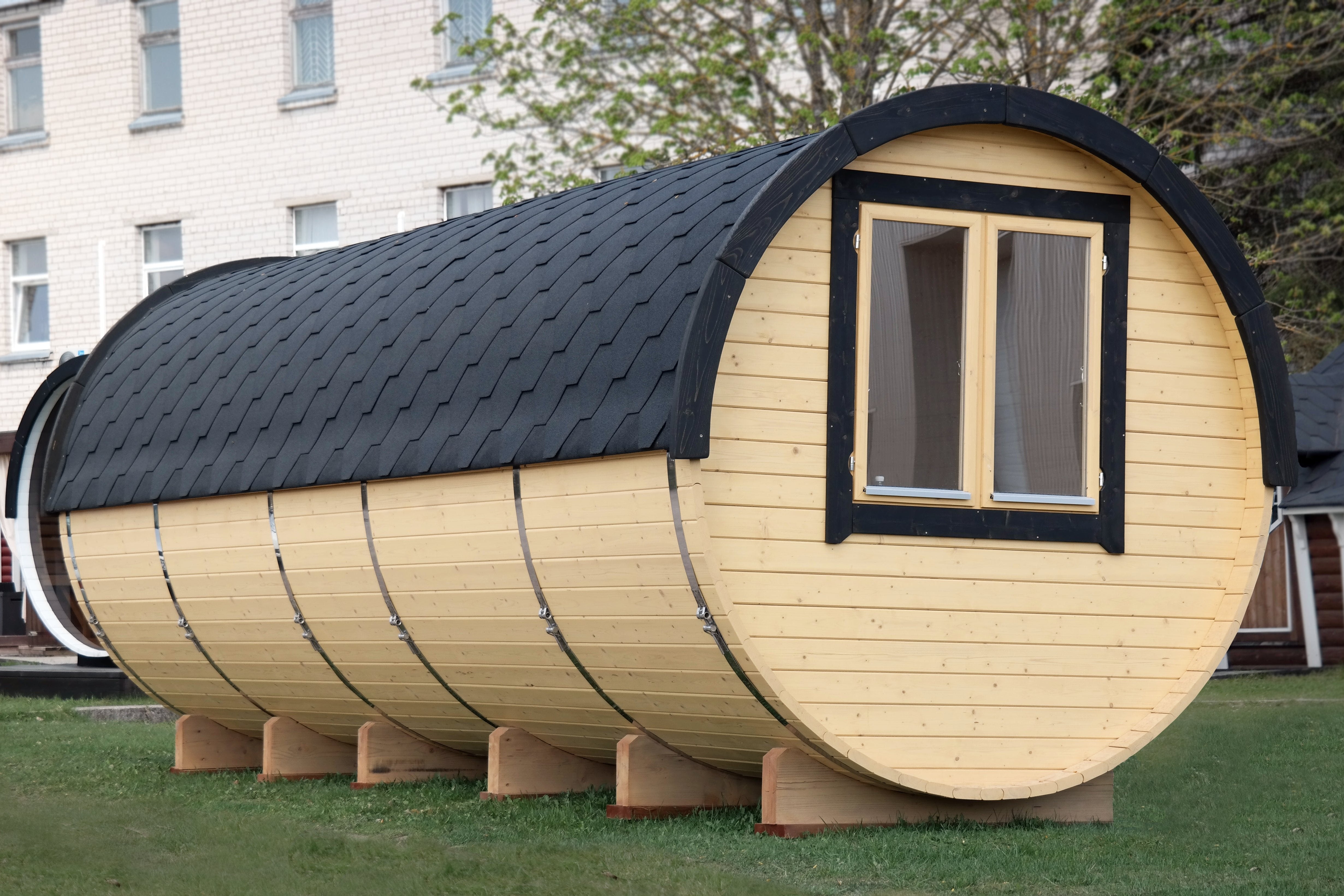 an angled photo showing the rear of a sauna barrel with a black shingled roof and a light oak finish on the wood.